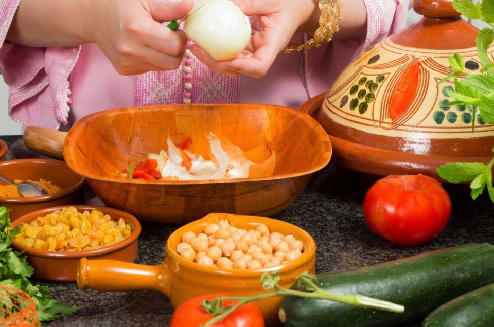 A closeup photo of hands chopping an onion into a bowl which sits next to a Moroccan tagine and other ingredients used in a cooking class in Casablanca.