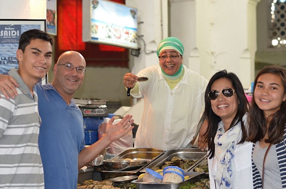 A mother, father and two teenagers pose with a woman fish vendor during a food tour at Marche Central in Casablanca.